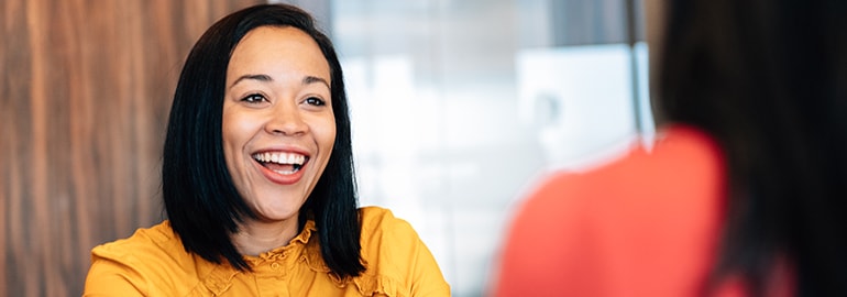 Two women engaged in conversation, one smiling warmly at the other