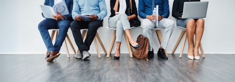 A line of job interview candidates waiting their turn while sitting on a chair.