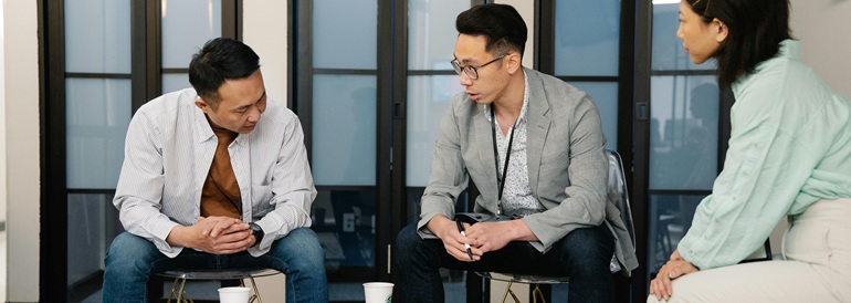 Three colleagues engaged in conversation around a table, discussing workplace flexibility and collaboration strategies.