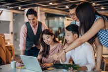 Several people engaged in teamwork around a laptop, demonstrating collaboration