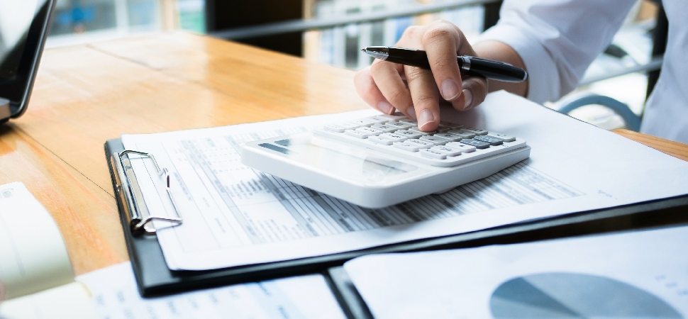 A person using a calculator on a desk, while looking at charts and numbers