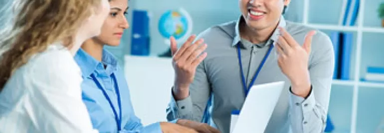 Three colleagues having a discussion at a table with a laptop.