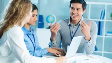 Three colleagues having a discussion at a table with a laptop.