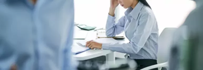 Woman in office looking stressed, seated at desk with papers.