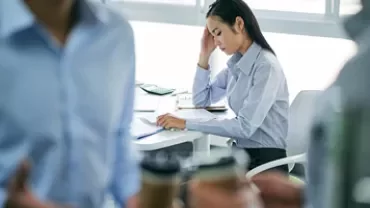 Woman in office looking stressed, seated at desk with papers.