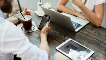 Two people working on electronic devices at an outdoor table.