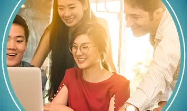 Group of four people happily looking at a laptop in a bright office.