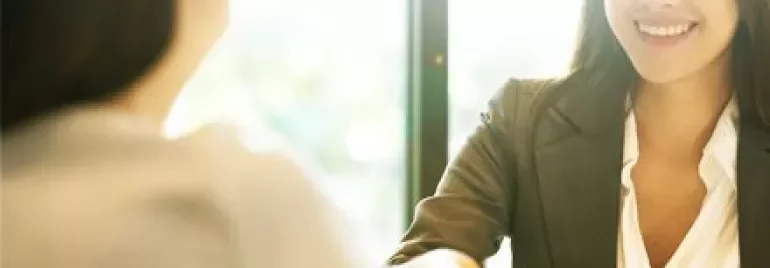 Two people shaking hands in a bright office setting.
