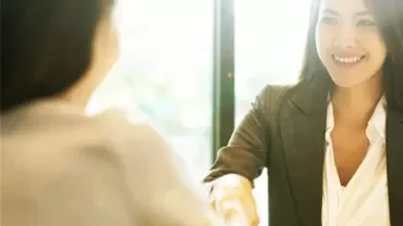 Two people shaking hands in a bright office setting.