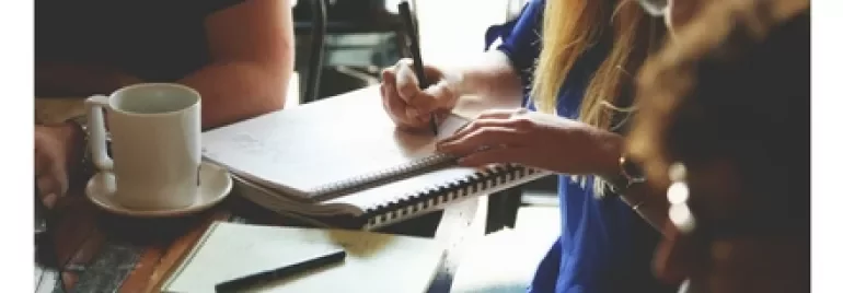 People discussing work around a table with notebooks and a laptop.