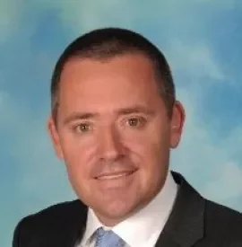 Portrait of a smiling man in a suit with a blue sky background.