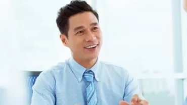 Smiling man in a blue shirt talking with a colleague in an office.