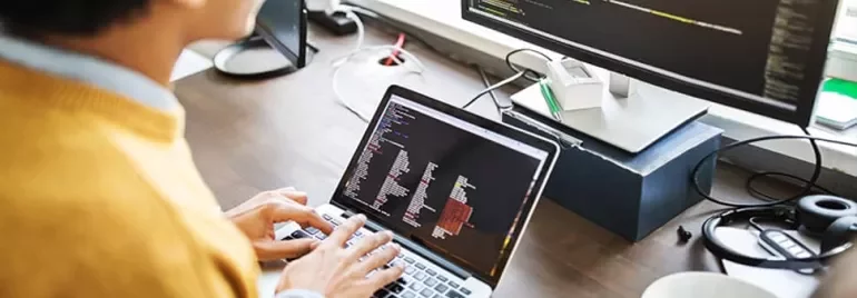 Person typing code on a laptop with a larger screen showing more code.