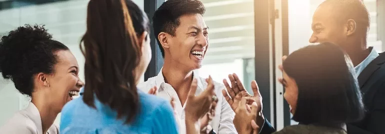Group of colleagues smiling and clapping in a meeting.