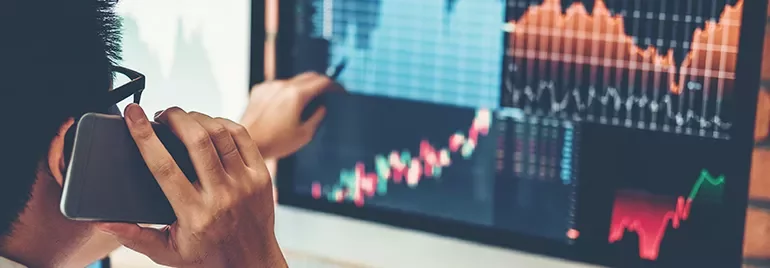Person analyzing financial charts on a computer screen, talking on the phone.