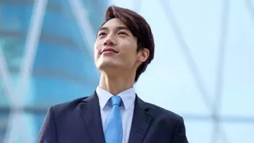Confident man in a suit looking up, blue building background.