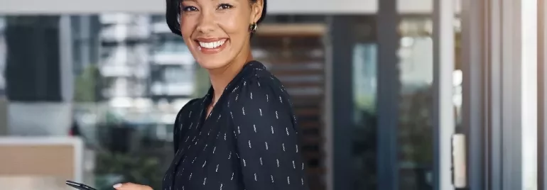 Smiling woman in a black blouse holding a smartphone indoors.
