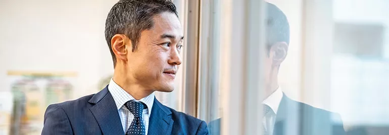 Man in a suit looking out the window with reflection visible.