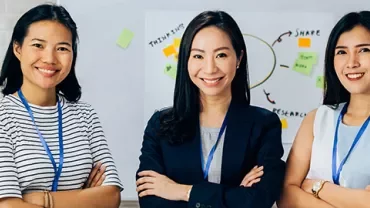 Three women smiling, standing in front of a whiteboard with sticky notes.