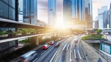 Sunrise over city with skyscrapers and blurred traffic, highlighting urban movement.