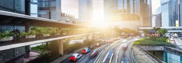 Sunrise over city with skyscrapers and blurred traffic, highlighting urban movement.