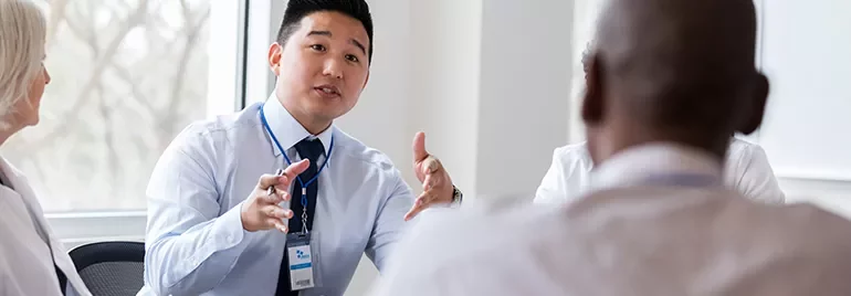A group of diverse professionals in a meeting room, one person is speaking passionately while others listen intently.
