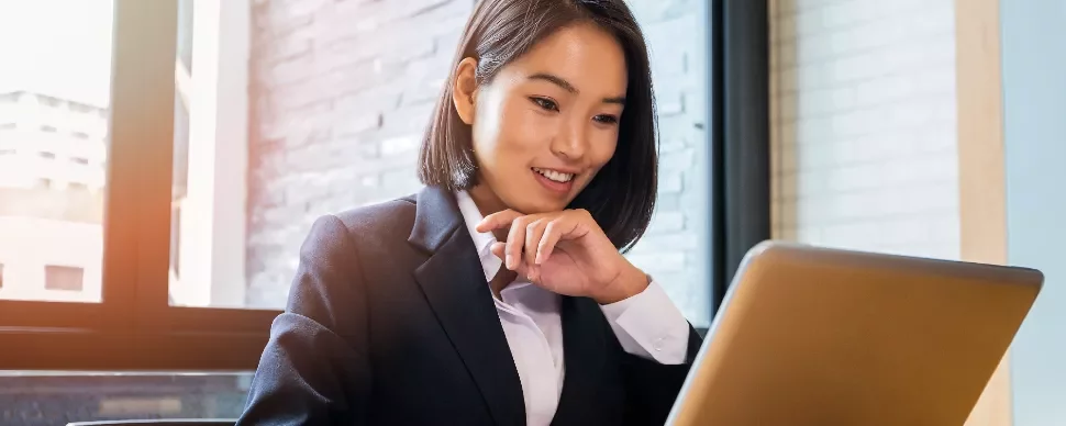 Businesswoman smiling while working on a laptop at her desk.