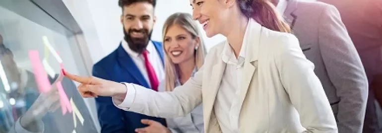 Smiling team collaborating and placing sticky notes on a glass board.