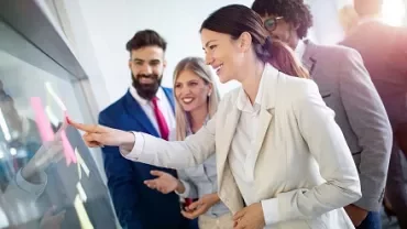 Smiling team collaborating and placing sticky notes on a glass board.