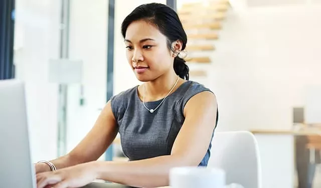 Woman working on a laptop in a bright office environment.