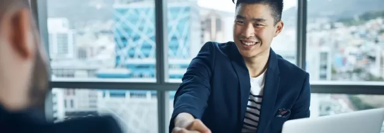 Smiling man in a suit shaking hands across a desk in an office.