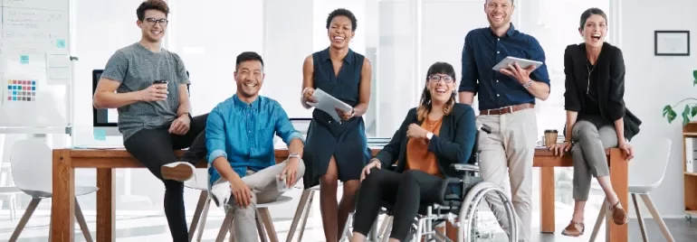 Diverse group of coworkers smiling in a bright office space around a table.