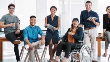 Diverse group of coworkers smiling in a bright office space around a table.