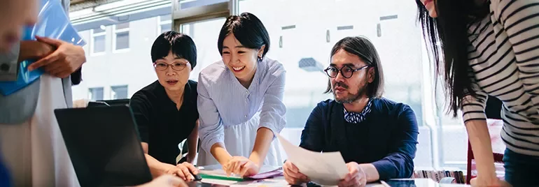 A diverse group of people collaborating around a laptop.