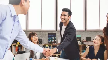 Group of professionals in a meeting, two men shaking hands.