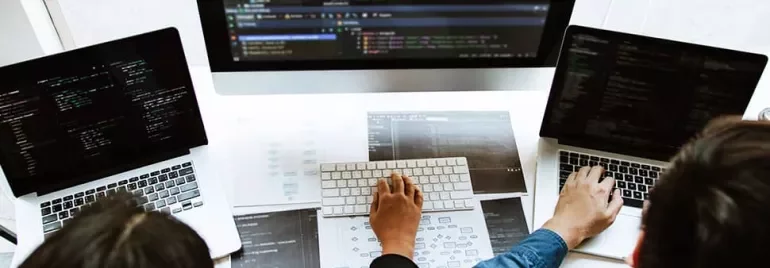 Three people working on laptops with code on screens.