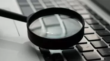 Magnifying glass on a laptop keyboard, symbolizing search or investigation.