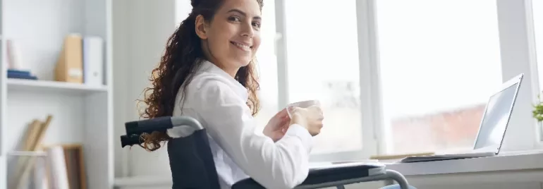 Woman in a wheelchair smiling while holding a mug by a window.
