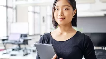 Woman in office holding tablet with large windows.