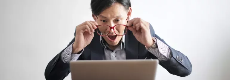 Man with glasses looking surprised at laptop screen.
