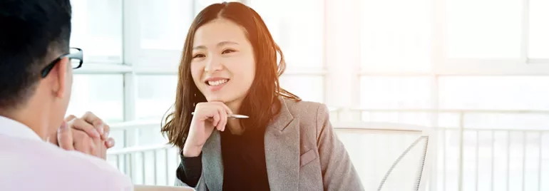 Woman in a gray blazer smiling during a meeting in a bright office.