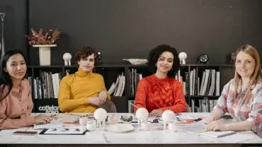 Four people sitting at a table in an office setting, with bookshelves in the background.