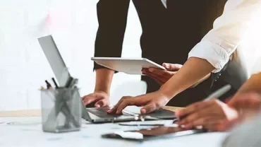 People working together at a desk with laptops and tablets.
