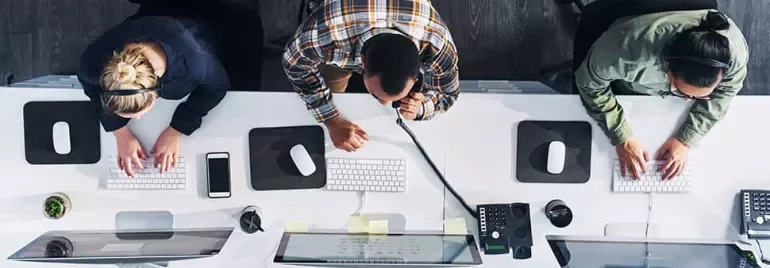 Three people working at computers in an office setting, viewed from above.