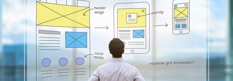 Man looking at wireframe sketches for desktop, tablet, and mobile designs on a clear board.