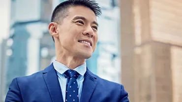 Smiling man in a blue suit stands confidently with city skyscrapers in the background.