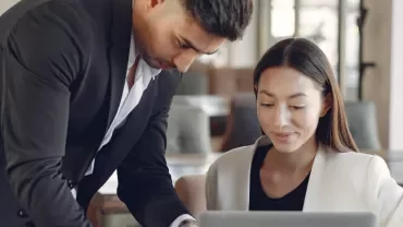 Two colleagues collaborating on a laptop in a modern office.