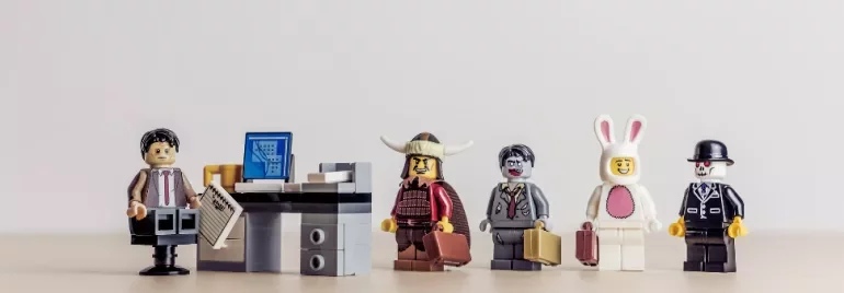 Lego figures dressed in various costumes standing in line at an office desk.