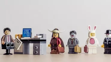 Lego figures dressed in various costumes standing in line at an office desk.