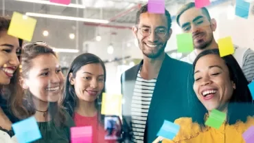 A diverse group of people brainstorming with colorful sticky notes on a glass wall.